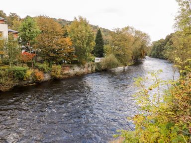 A river with trees and buildings along the bank at The Garden Hut in Wrexham