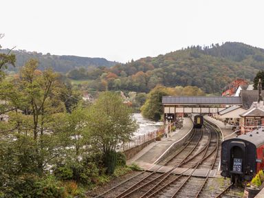 A train station with railway tracks and a river at The Garden Hut in Wrexham