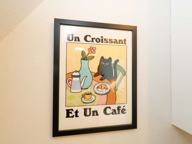 A framed artwork featuring a cat, coffee, and croissant in the dining room at Seagull & Chips in Weymouth