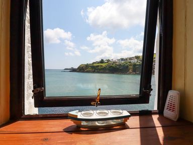 A window open to a sea view with a coastal hill and houses at Rock Cottage in Portmellon near Mevagissey
