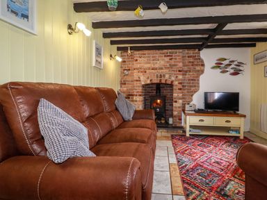 A living room with a brown couch a fireplace a television on a cabinet and a colorful rug at Rock Cottage in Portmellon near Mevagissey