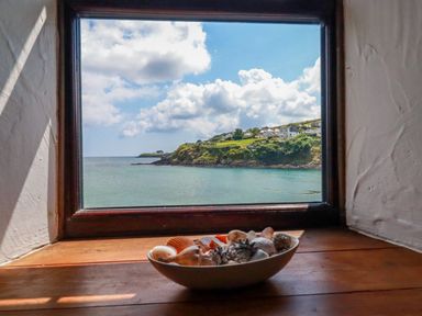 A bowl of seashells on a wooden windowsill overlooking a coastal view at Rock Cottage in Portmellon near Mevagissey