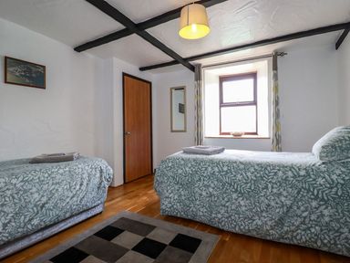 A bedroom with two single beds with patterned bedspreads a wooden door a window with curtains and a mirror on the wall at Rock Cottage Portmellon near Mevagissey