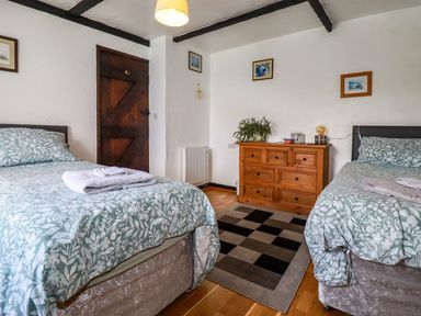 A bedroom with two single beds a wooden chest of drawers and a patterned rug at Rock Cottage in Portmellon near Mevagissey