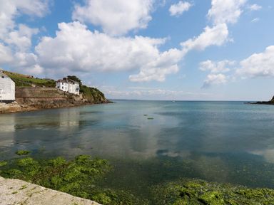 A coastal scene with houses on a rocky shore and seaweed in the water at Rock Cottage in Portmellon near Mevagissey