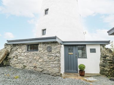 A lighthouse with a stone wall and door at The Old Cornmill Cemaes Bay