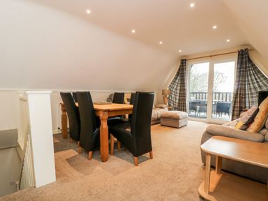 A dining area with a wooden table and black chairs next to a living space with sofas and a balcony at Valley Lodge 31 in St Ann's Chapel Cornwall