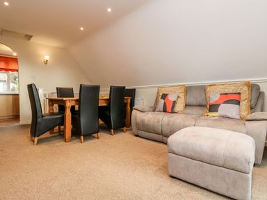A living room with a gray sofa and ottoman with patterned cushions and a wooden dining table with black chairs at Valley Lodge 31 in St Ann's Chapel Cornwall