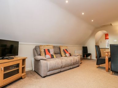 A living room with a sofa a TV on a wooden stand a wooden dining table with black chairs and an arched doorway at Valley Lodge 31 in St Ann's Chapel Cornwall