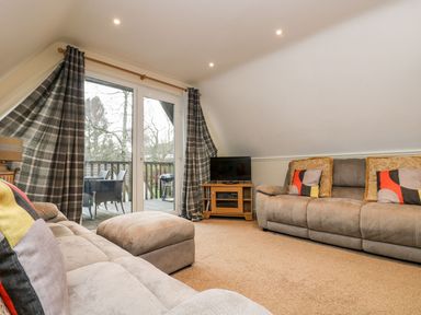A living room with sofas a television and patio doors opening to a balcony at Valley Lodge 31 in St Ann's Chapel Cornwall