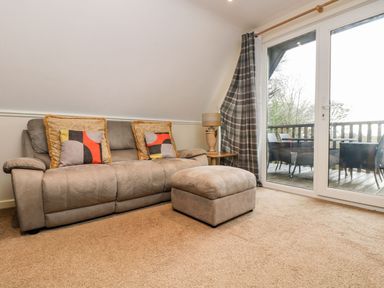 A seating area with a sofa with patterned cushions an ottoman a table lamp a side table and glass doors leading to a balcony at Valley Lodge 31 in St Ann's Chapel Cornwall