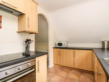 A kitchen with wooden cabinets black countertops a microwave oven a built in stove and tiled floor at Valley Lodge 31 in St Ann's Chapel Cornwall