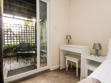 A bedroom with a white desk and two lamps next to a glass door opening to a small balcony with two chairs and a table at Valley Lodge 31 St Ann's Chapel Cornwall