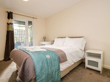 A bedroom with a double bed a bedside table with a lamp and a door with curtains at Valley Lodge 31 in St Ann's Chapel Cornwall