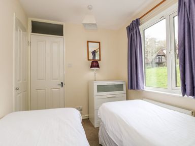A bedroom with two single beds a white chest of drawers a lamp a mirror and a window with purple curtains at Valley Lodge 31 in St Ann's Chapel Cornwall