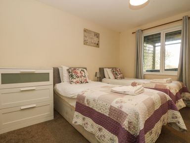 A bedroom with two single beds with floral pillows and quilted bedspreads a white chest of drawers and a window with curtains at Valley Lodge 31 in St Ann's Chapel Cornwall