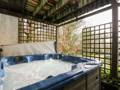 An outdoor covered hot tub with lattice panels and trees in the background at Valley Lodge 31 in St Ann's Chapel Cornwall