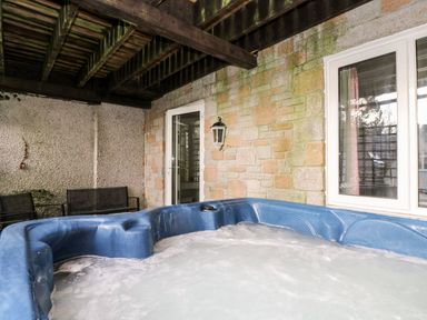 An outdoor covered patio area with a blue hot tub and black chairs at Valley Lodge 31 in St Ann's Chapel Cornwall