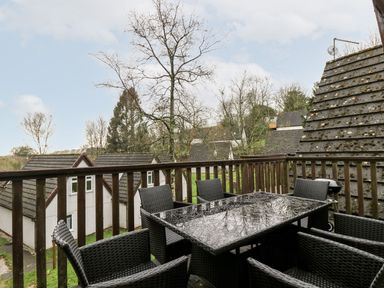 A balcony with a glass top table and six wicker chairs overlooking houses and trees at Valley Lodge 31 in St Ann's Chapel Cornwall