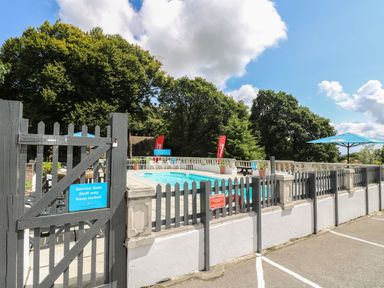 Outdoor swimming pool area with grey fence and safety signs surrounded by trees at Valley Lodge 31 in St Ann's Chapel Cornwall