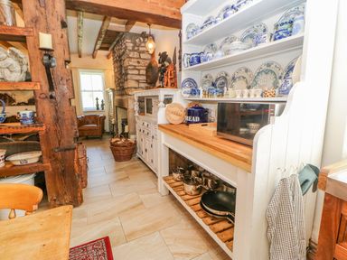 A kitchen with wooden beams plates on shelves a microwave and pots on a shelf at Shaftoe Mews in Haydon Bridge
