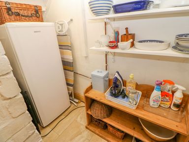 A utility room with a white freezer iron and cleaning products on wooden shelves at Shaftoe Mews in Haydon Bridge