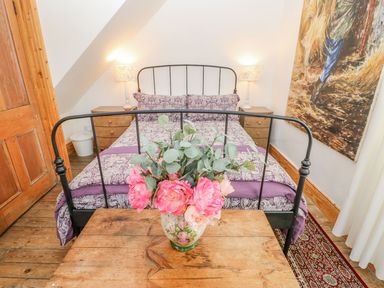 A bedroom with a metal bed frame a wooden table with a flower vase and a painting on the wall at Shaftoe Mews in Haydon Bridge