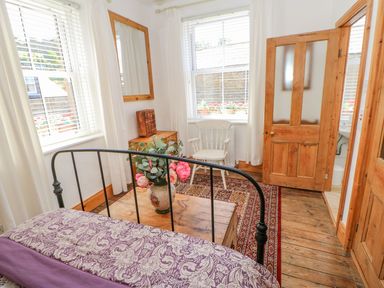A bedroom with a metal bed frame wooden chest flowers on chest a white chair a mirror on the wall and wooden doors at Shaftoe Mews in Haydon Bridge