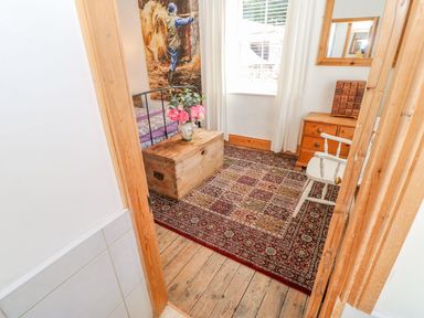 A bedroom with a wooden chest with flowers on top a patterned rug wooden furniture and a window with white curtains at Shaftoe Mews in Haydon Bridge