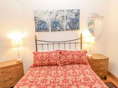 A bedroom with a bed with red patterned bedding between two wooden nightstands with lamps and a decorative mirror on the wall at Shaftoe Mews in Haydon Bridge