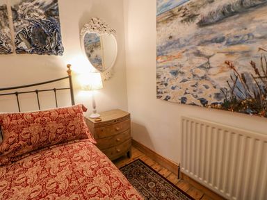 A bedroom corner with a bed covered in red floral bedding a wooden nightstand with a lamp and a white decorative mirror on the wall at Shaftoe Mews in Haydon Bridge