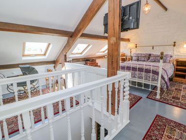 An attic bedroom with a white railing wooden beams skylight windows a bed with purple bedding and vintage furniture at Shaftoe Mews in Haydon Bridge