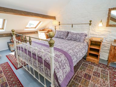 A bedroom with a wooden bed covered with purple patterned bedding next to wooden furniture and rugs at Shaftoe Mews in Haydon Bridge