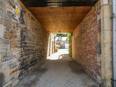 A stone and brick covered passageway with gravel floor leading to a building with plants and flowers at Shaftoe Mews in Haydon Bridge