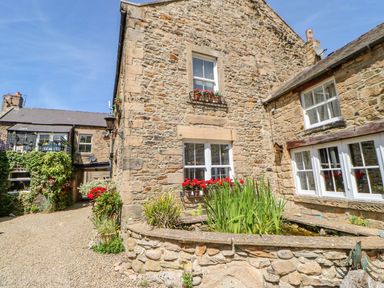 A stone house with white-framed windows and flower boxes on a gravel path at Shaftoe Mews in Haydon Bridge