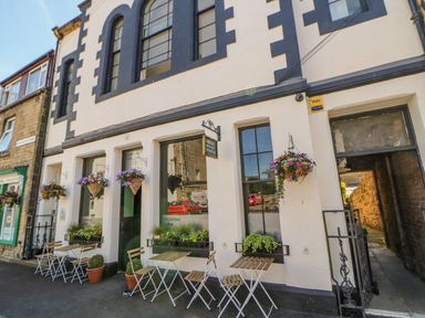 An outdoor seating area with tables and chairs and hanging flower baskets outside a coffee shop on a street