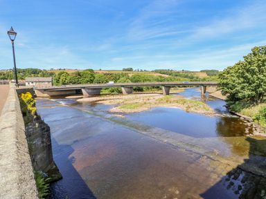 A river flowing under a bridge with vehicles and greenery in the background at Shaftoe Mews in Haydon Bridge