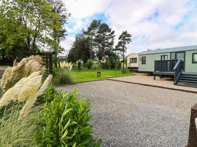 A grassy area with gravel and a caravan at Ava Lodge in West Mains near Haggerston