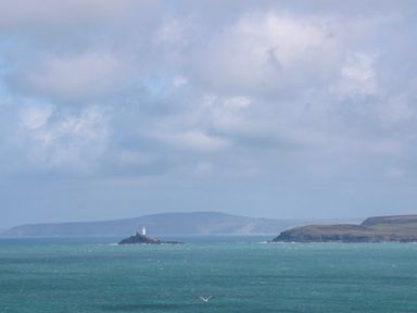 A lighthouse on an island in the ocean with clouds at The Cottage in St. Ives