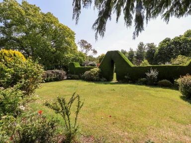 A garden with a hedge and flower beds at Rose Cottage in Dunstan near Embleton