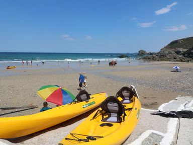A beach with kayaks and people walking at Carn Brea Redruth