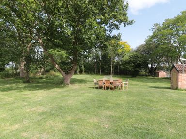 A garden with a table and chairs surrounded by trees at 1 The Stables in Highbridge