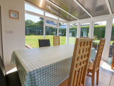 A conservatory with a table and chairs overlooking the garden at Swn Y Don
