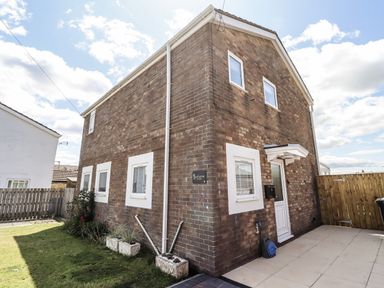 A brick house with a garden and pathway at Seahorse Cottage in Chathill