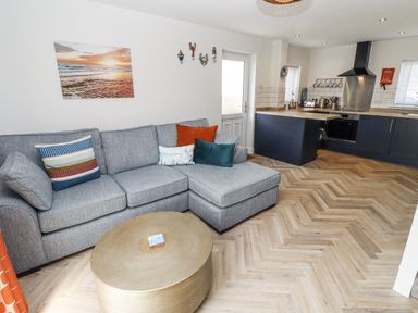 A living room with a sofa and kitchen area at Seahorse Cottage in Chathill
