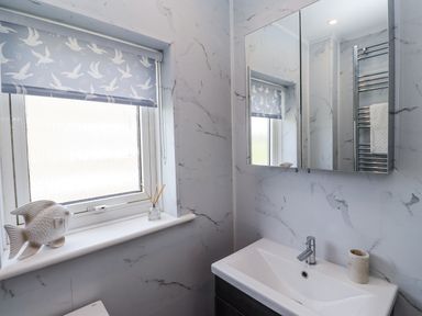 A bathroom with a sink, mirror, and window at Seahorse Cottage in Chathill
