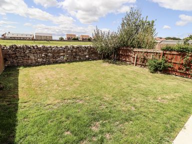 A garden with grass and a stone wall at Seahorse Cottage in Chathill