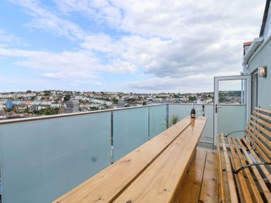 A balcony with a wooden table and chairs overlooking Brixham