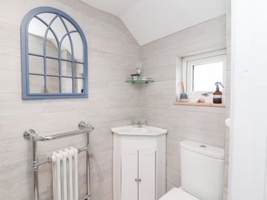 A bathroom with a mirror, hand basin, toilet and window at Still Waters in Brixham