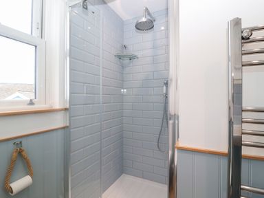 A shower enclosure with glass wall and tiled walls at Still Waters in Brixham